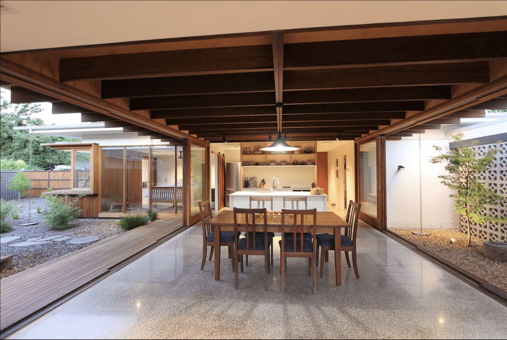 Image shows a dining room with large floor to ceiling windows either side. 