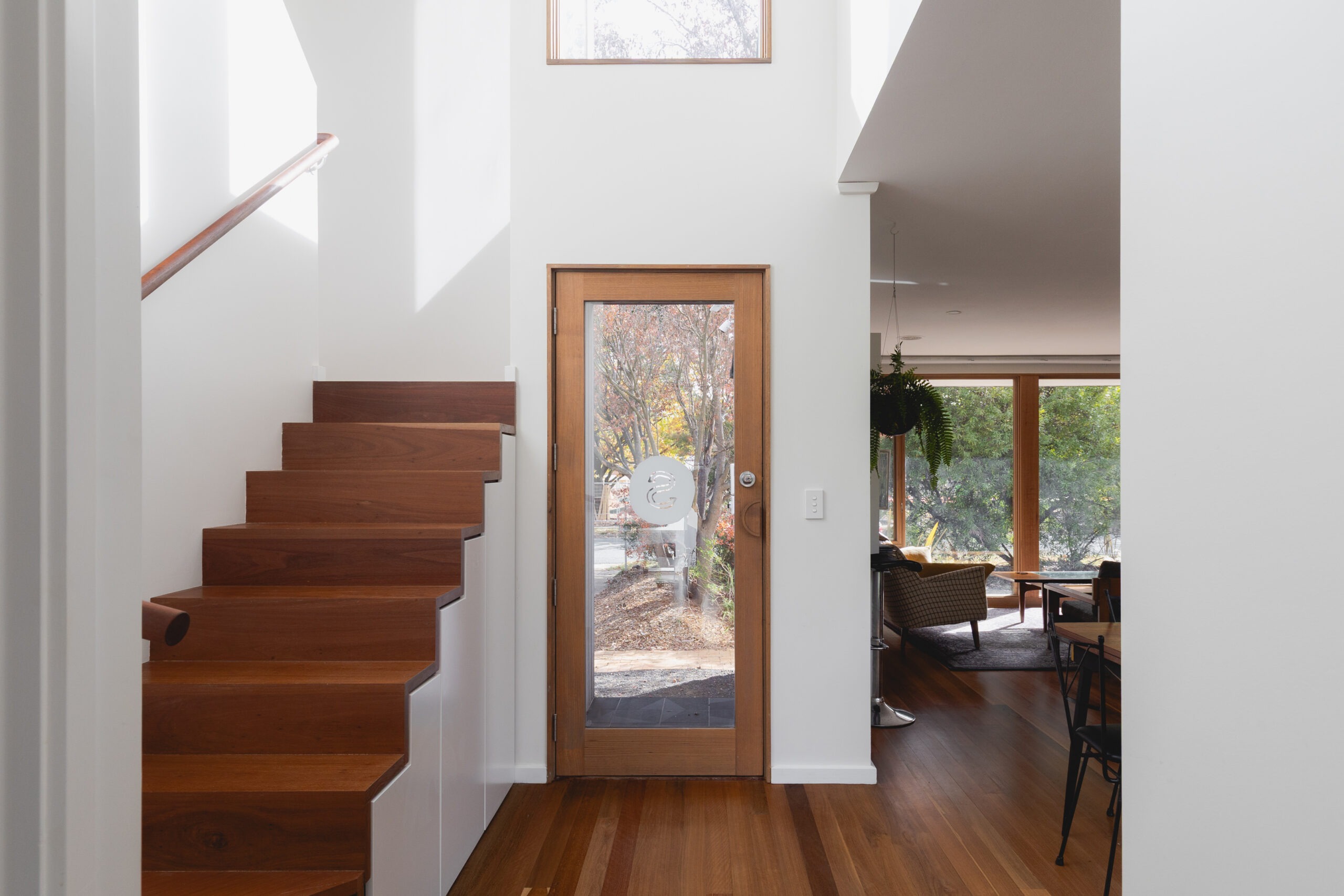 Timber staircase beside a glazed entry door in a light-filled interior.