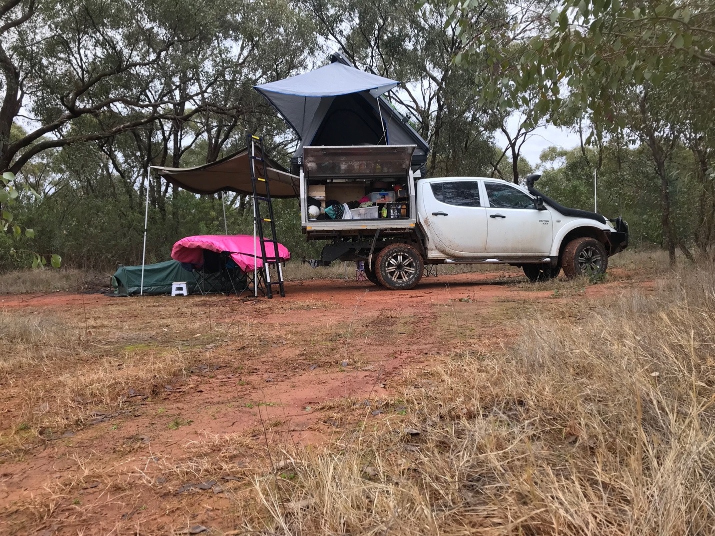 A rooftop tent and two swags set up beside a ute in the Australian bush.