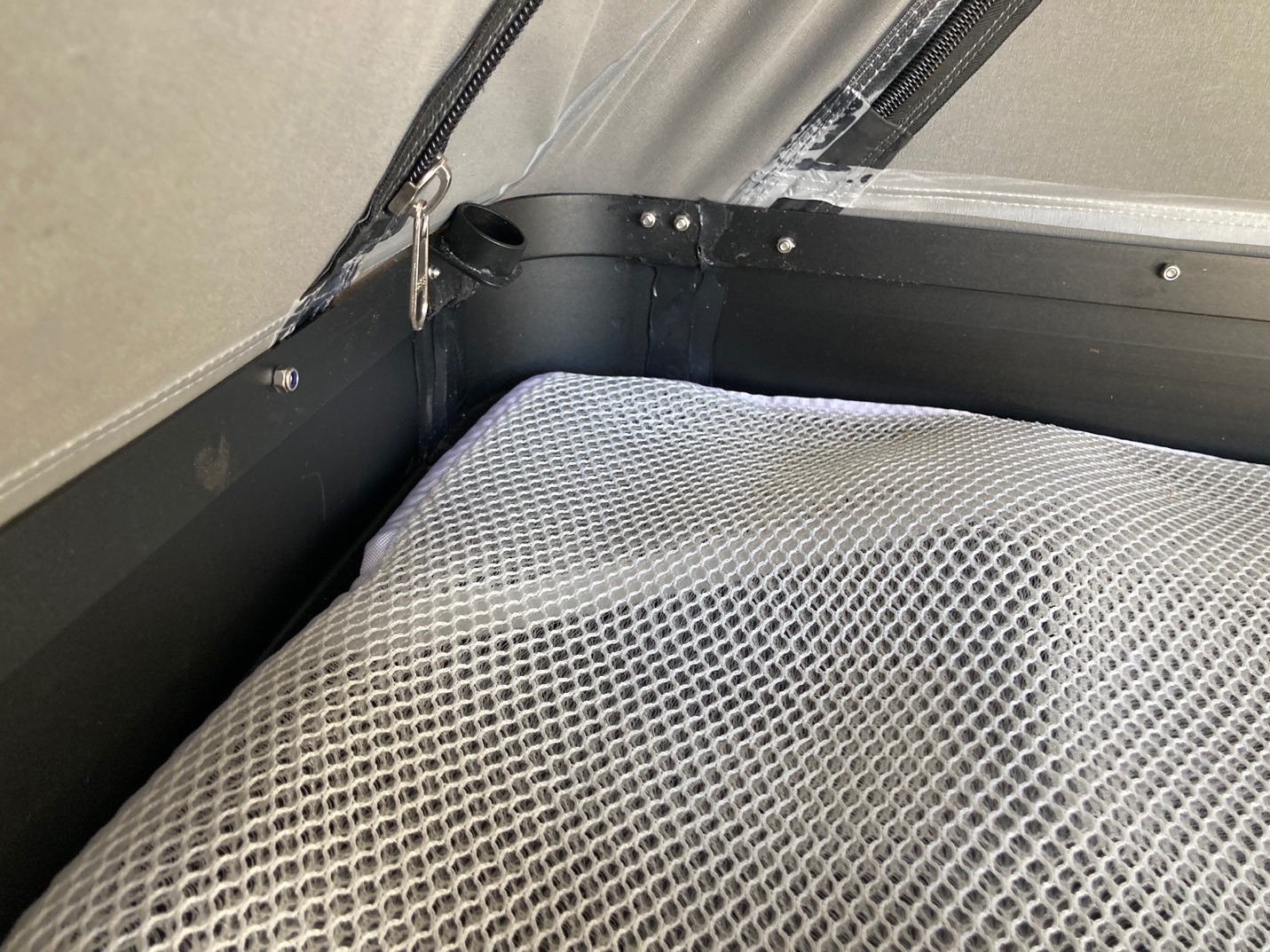 A mesh spacer lying above the aluminium floor inside a rooftop tent.